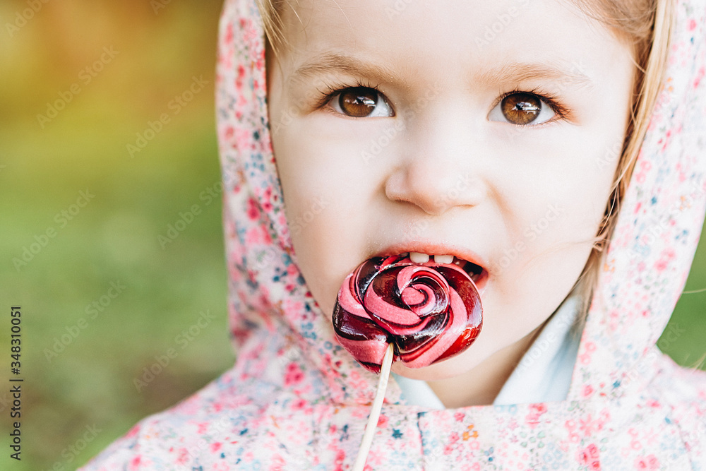little 3yearold girl licks a colored swirling candy on a walk in the