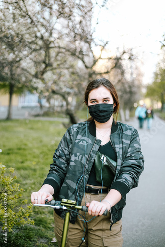 Girl in a protective black mask on a scooter in the street 