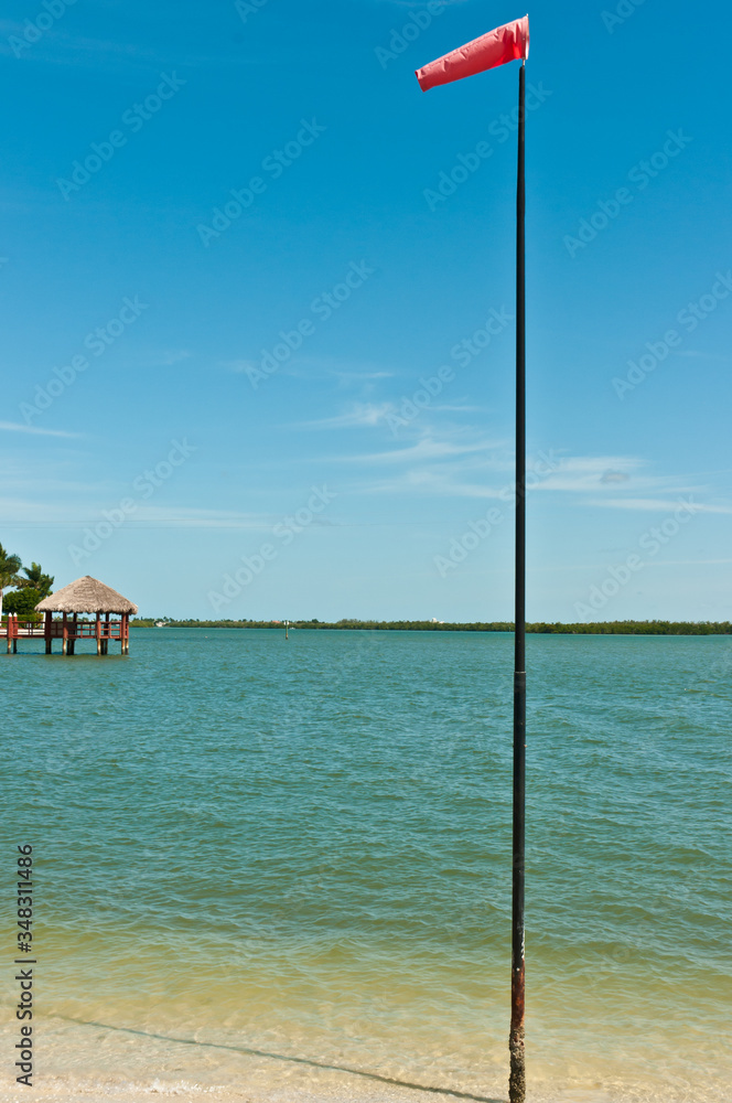 Front view, medium distance of a wind sock on a tall pole, at a tropical marina to measure wind speed and direction to provide information to help sailing ships personal safety for people and sailboat