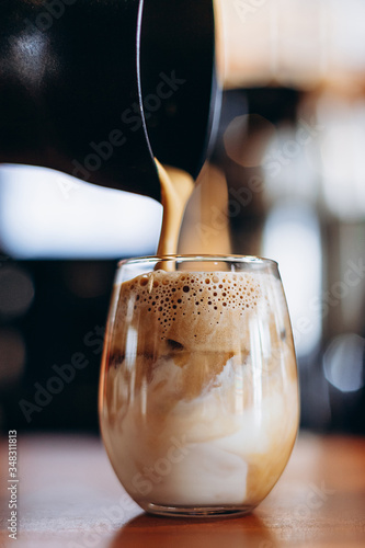 transparent glass with foamy coffee with milk and ice, summer version of Dalgano coffee on the bar table in a cafe photo