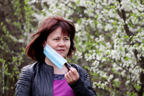 Joyful woman removing medical protective mask in a spring garden on cherry blossom background. Concept of enjoying the flowers smell, fresh air, end of the quarantine during covid-19 coronavirus pande photo