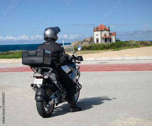 Motociclista a passear  parado a observar o mar e uma pequena igreja constru  da numa rocha dentro do mar  Senhor da Pedra