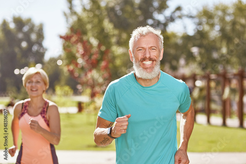 Staying healthy and fit. Happy mature man smiling at camera while running together with his wife in the early morning. Selective focus