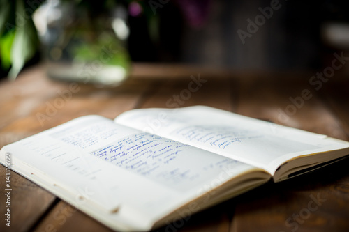open recipe journal with notes on a wooden table with flower in the background