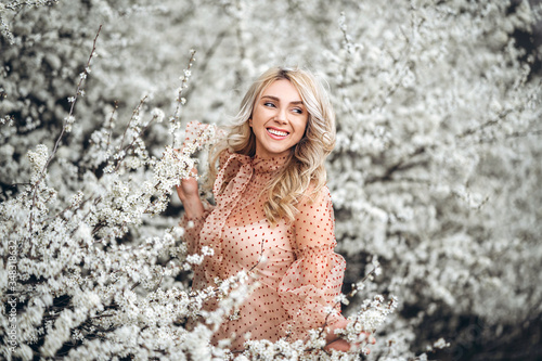 Woman with gorgeous smile, curly blond hair in red dress having fun in blooming garden
