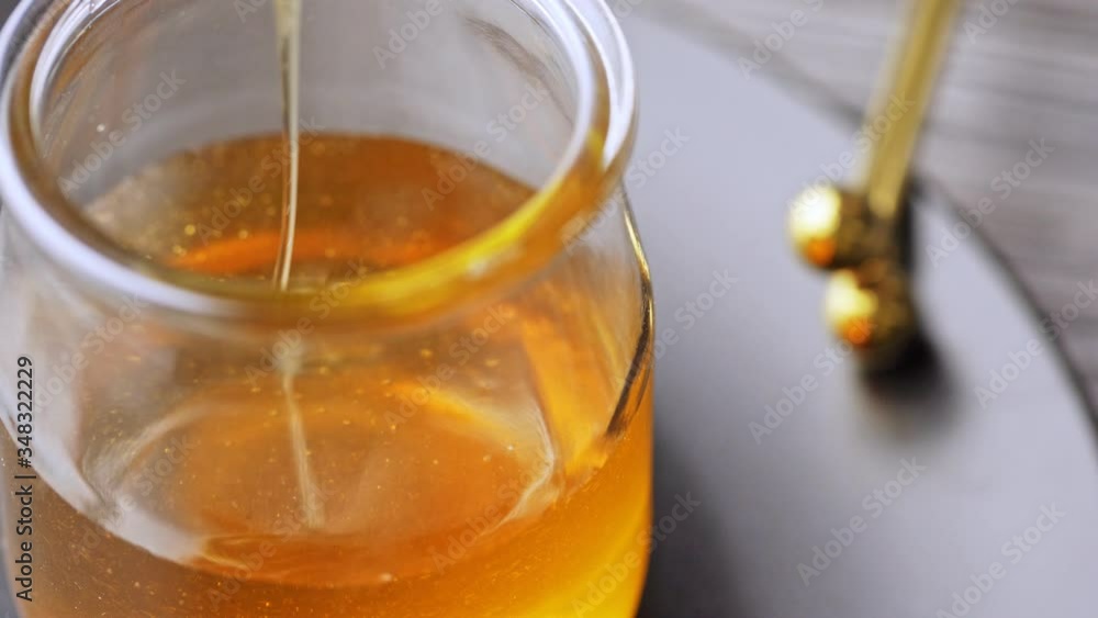Liquid organic raw honey in glass jar with metal honey dipper. Liquid organic raw honey in glass jar with metal honey dipper.