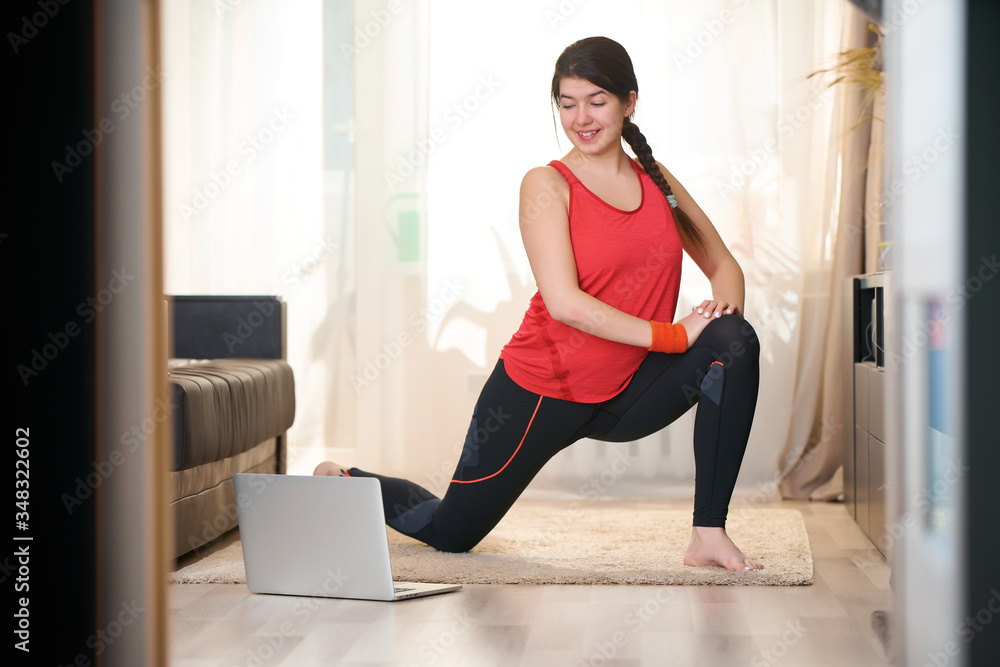 Woman is doing stretching, practicing yoga exercises at home using video tutorials.