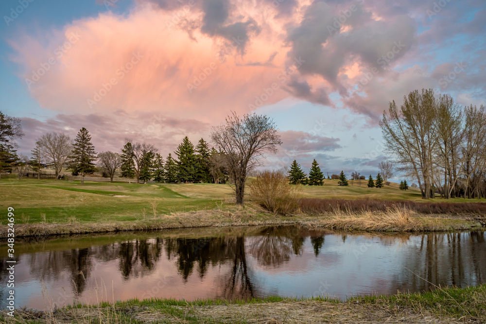 Towering pink sunset cloud over the Swift Current Creek on a golf course in Swift Current, SK, Canada