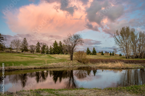 Towering pink sunset cloud over the Swift Current Creek on a golf course in Swift Current, SK, Canada