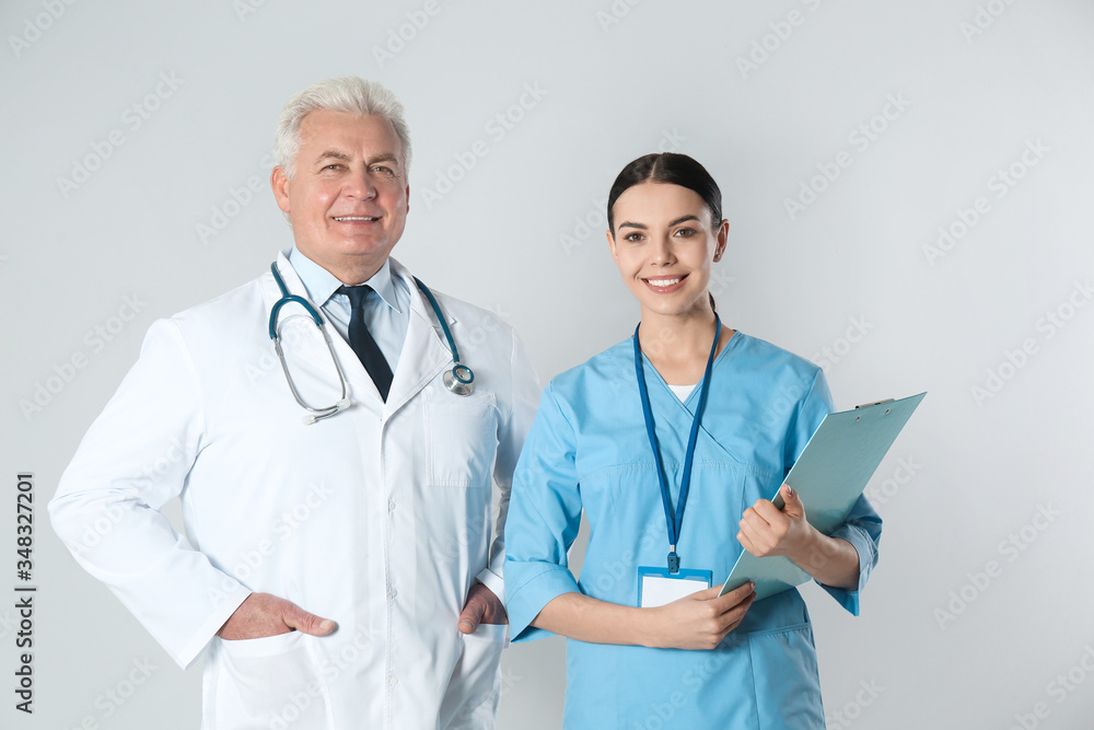 Senior doctor and young nurse against light background Senior doctor and young nurse against light background