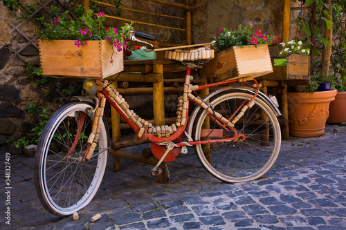 A classic red bike is decorated with wine corks and crates on a cobblestone street in Orvieto, Italy