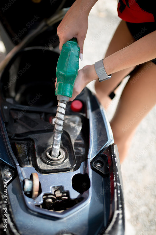 Obraz premium Female hands with a hose pours gasoline into a gas tank of a bike close-up.