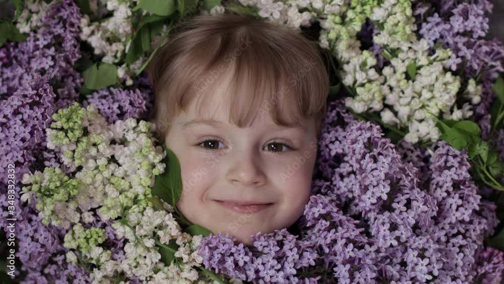 Cute girl child looking from bunch bouquet of lilac flowers around her face Cute girl child looking from bunch bouquet of lilac flowers around her face