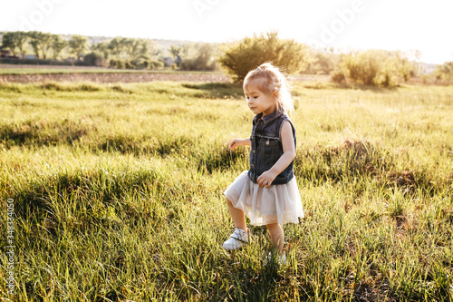 Little girl walking, running in a meadow with fresh green grass on a summer day at the sunset.