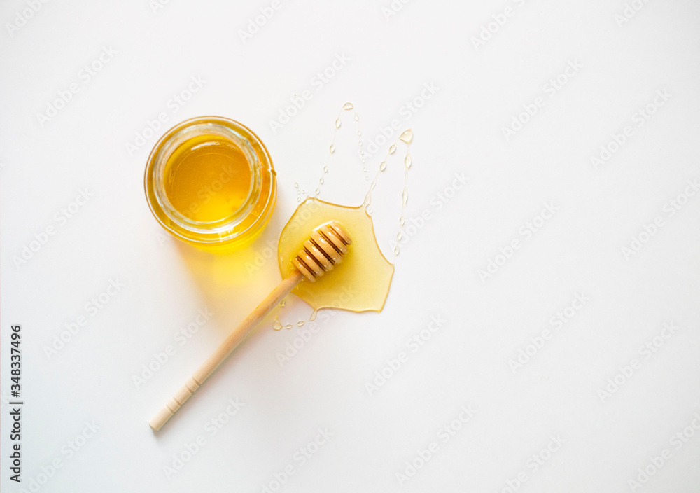 glass jar with honey and with a wooden honey stick on a white background.
