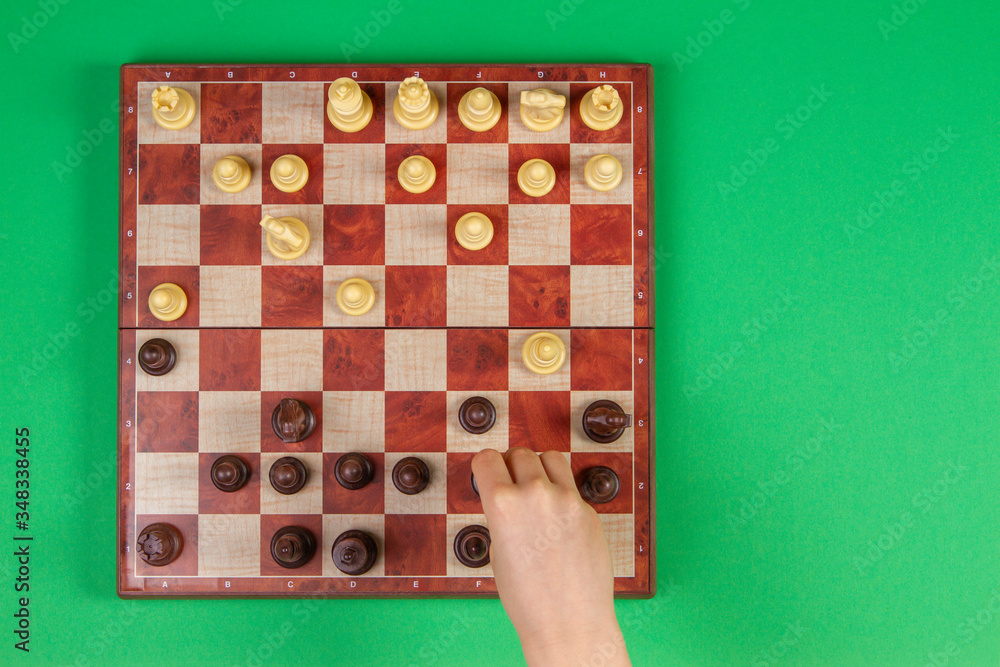 Kid hand moving chess figure, playing chess game. Chessboard on light green background, top view Kid hand moving chess figure, playing chess game. Chessboard on light green background, top view