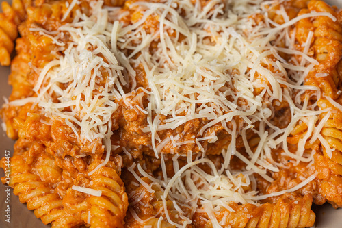 Bolognese pasta served on a brown plate with grated cheese close up still