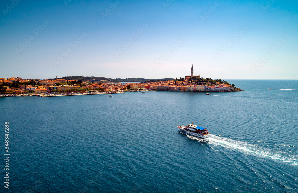 A boat with tourists is heading through the Rovinj.  Aerial view taken by a professional drone from above the sea. The old town of Rovinj and Adriatic sea, Istria, Croatia