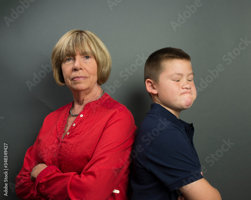 Preteen boy showing stubborn express with back to mother who is also showing no inclination to change her mind. 