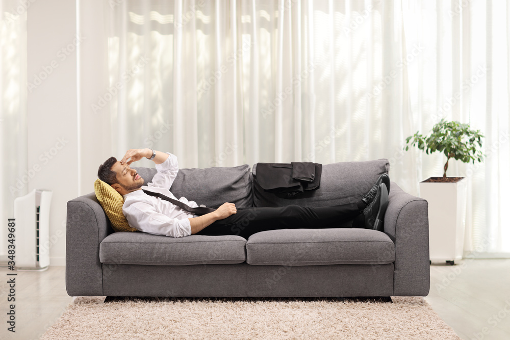 Fototapeta premium Tired man holding his head and lying on a couch at home
