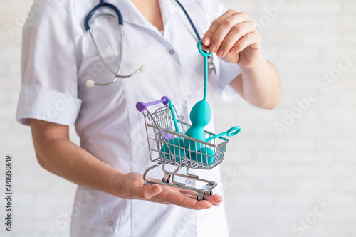 A faceless gynecologist puts a set of kegel balls into a miniature shopping cart. The doctor holds a mini trolley and device for vaginal muscles. Female health concept.