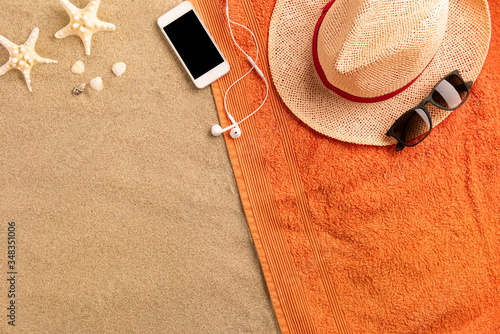 Top view straw hat and smartphone with copy space. Traveler accessories on sand. Travel vacation concept. Summer background. Border composition made of towel