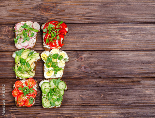 Variety of mini sandwiches with cream cheese and vegetables on a wooden background.
