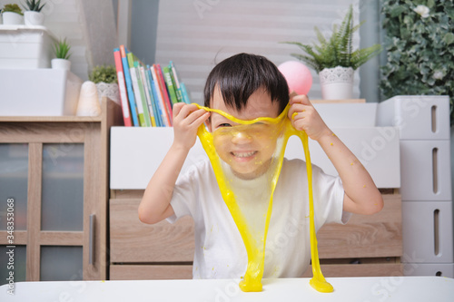 Cute happy smiling Asian 4 years old Kindergarten school boy having fun making yellow fluffy slime, Young kid having fun playing and being creative by science experiment homemade toy called Slime photo