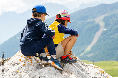 little boy and girl sit on a rock and look at the mountains. brother and sister are relax on the mountain and enjoying view of nature