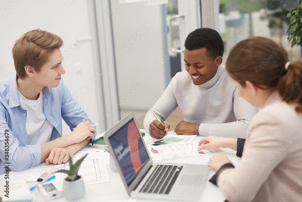 Group of young business people discussing work project and smiling cheerfully during meeting in office, copy space Group of young business people discussing work project and smiling cheerfully during meeting in office, copy space