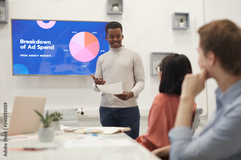 Obraz premium Portrait of young African man giving presentation on marketing during business meeting in modern office, copy space