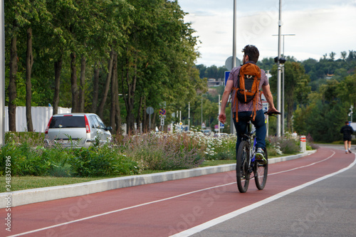 A man on a bicycle with a backpack rides on a track in a city park.