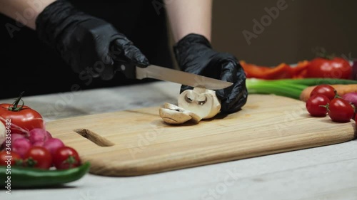 Woman slices fresh champignon mushrooms on the old wooden cutting board in the kitchen