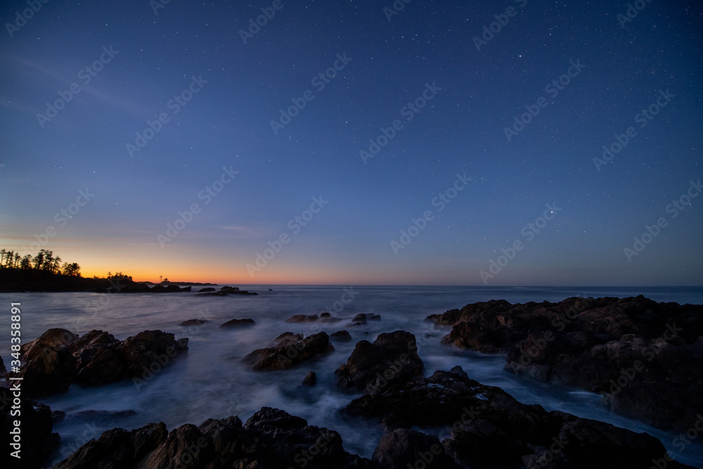 Ocean surf streams over black rocks at  sunrise.