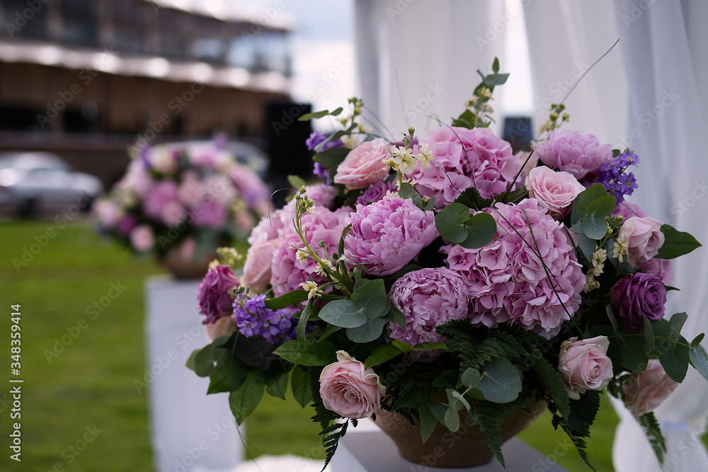 a large vase of flowers stands on a white pedestal in the park, a wedding decoration, a festive decor on the nature, pink flowers in a lush bouquet