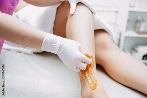 Beautician depilating young woman's legs with liquid sugar in spa center.
