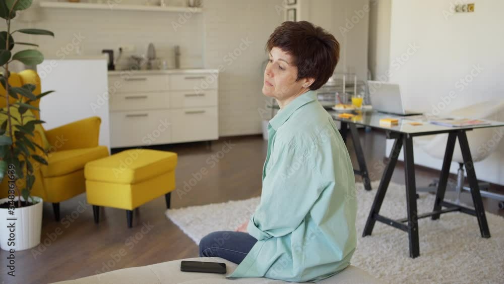 Anxious middle aged woman sitting on sofa at home with cell phone in her hands and touching herself nervously while awaiting for important call or text message Anxious middle aged woman sitting on sofa at home with cell phone in her hands and touching herself nervously while awaiting for important call or text message