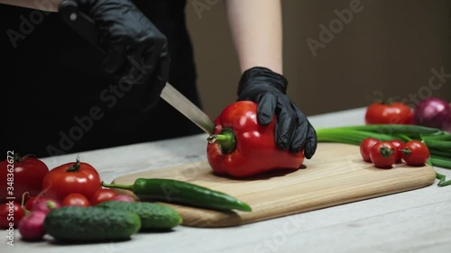 Hands in black gloves cutting red paprika pepper on wooden board in the kitchen