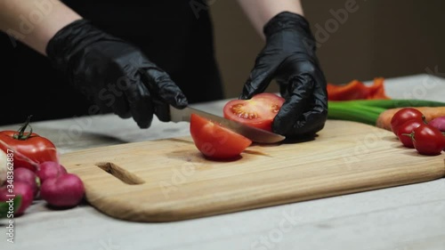 Hands in black gloves slices tomato on wooden board