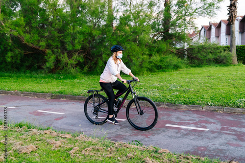 A woman on a bicycle with a safety mask on her face circulates on a bicycle path with houses in the background