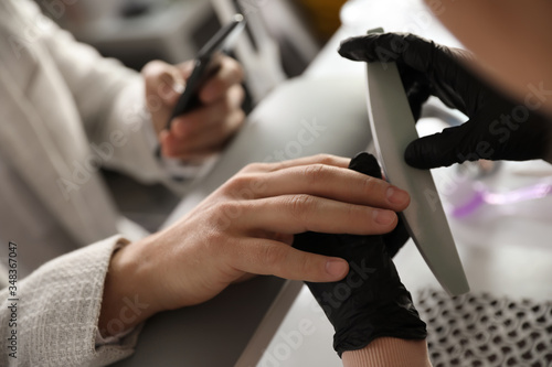 Professional manicurist filing client s nails in beauty salon  closeup