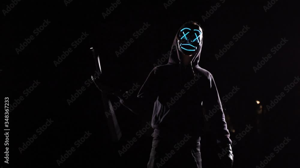 A man with a baseball bat in a mysterious glowing mask. Anonymous swings on a black background with light mask. A man with a baseball bat in a mysterious glowing mask. Anonymous swings on a black background with light mask.