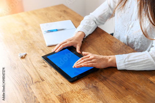 Close-up female hands in formal white shirt touch a digital tablet with a blank screen, a notebook with a pen for notes is near