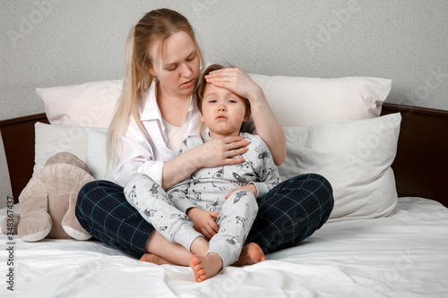 Mother hugs and measures the temperature of the child. The theme of the coronavirus. To remove a fever and chills