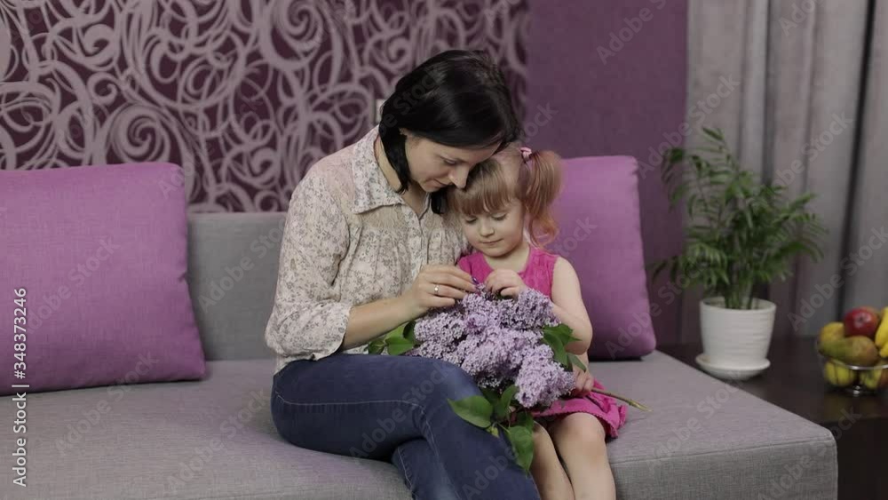 Little daughter and mother sitting on sofe with bouquet of lilac purple flowers Little daughter and mother sitting on sofe with bouquet of lilac purple flowers