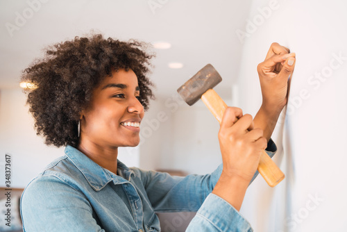 Fotografia, Obraz Afro woman hammering nail on the wall. Stay at home concept.