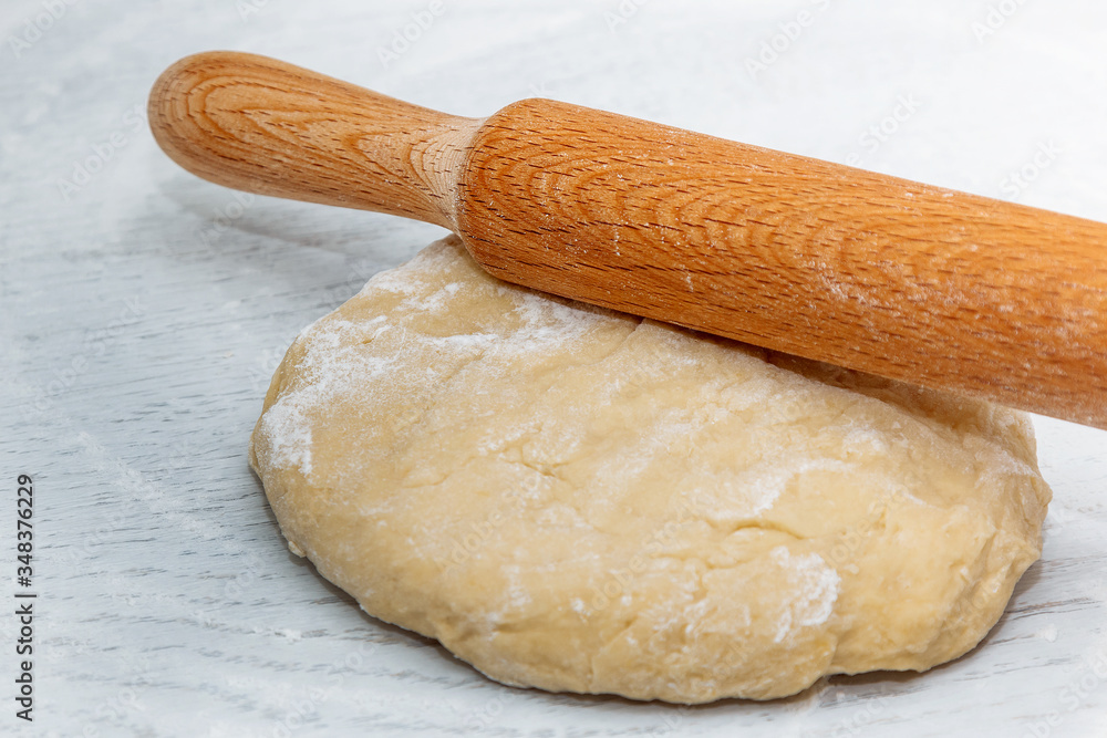 dough and rolling pin on the white kitchen table. the concept of home cooking. cooking homemade dough. close up dough and rolling pin on the white kitchen table. the concept of home cooking. cooking homemade dough. close up
