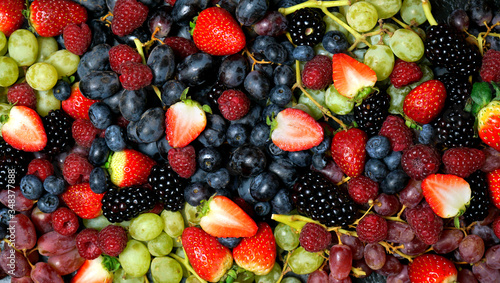 Summer berries food background full frame close up with strawberries  blackberries  blueberries  red  dark and green grapes on black marble.