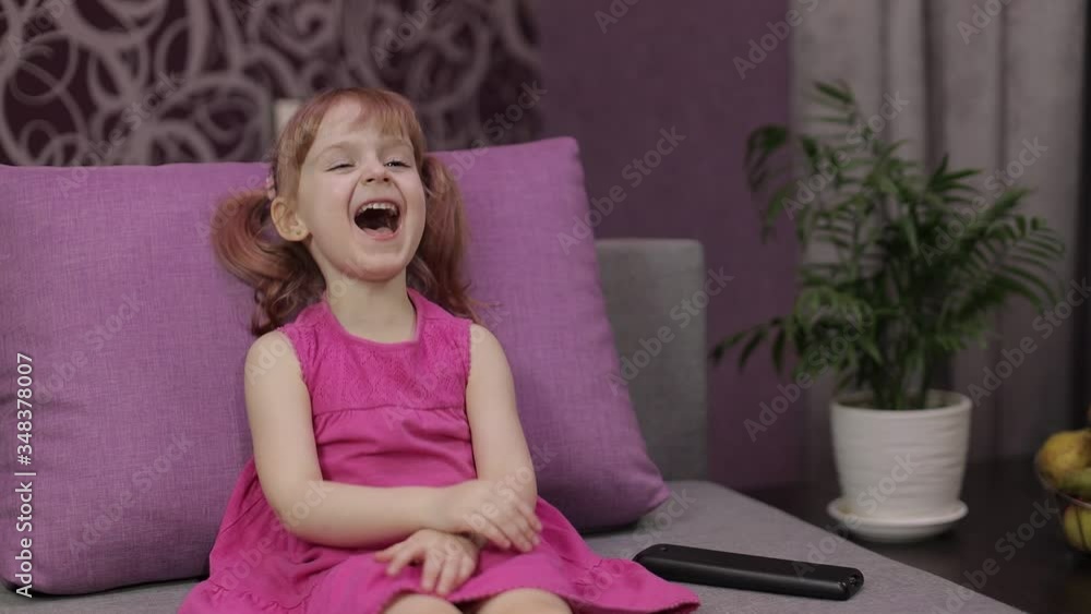 Little child sitting while watching TV. Happy kid girl watch funny music movie Little child sitting while watching TV. Happy kid girl watch funny music movie