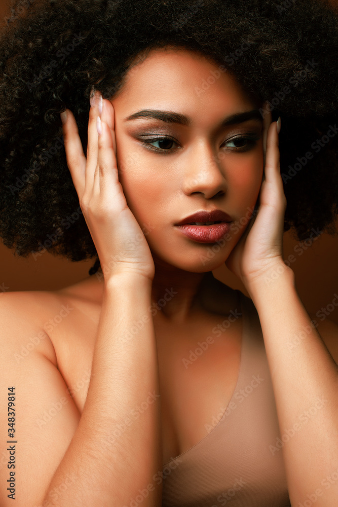 pretty young african american woman with curly hair posing cheerful gesturing on brown background, lifestyle people concept pretty young african american woman with curly hair posing cheerful gesturing on brown background, lifestyle people concept